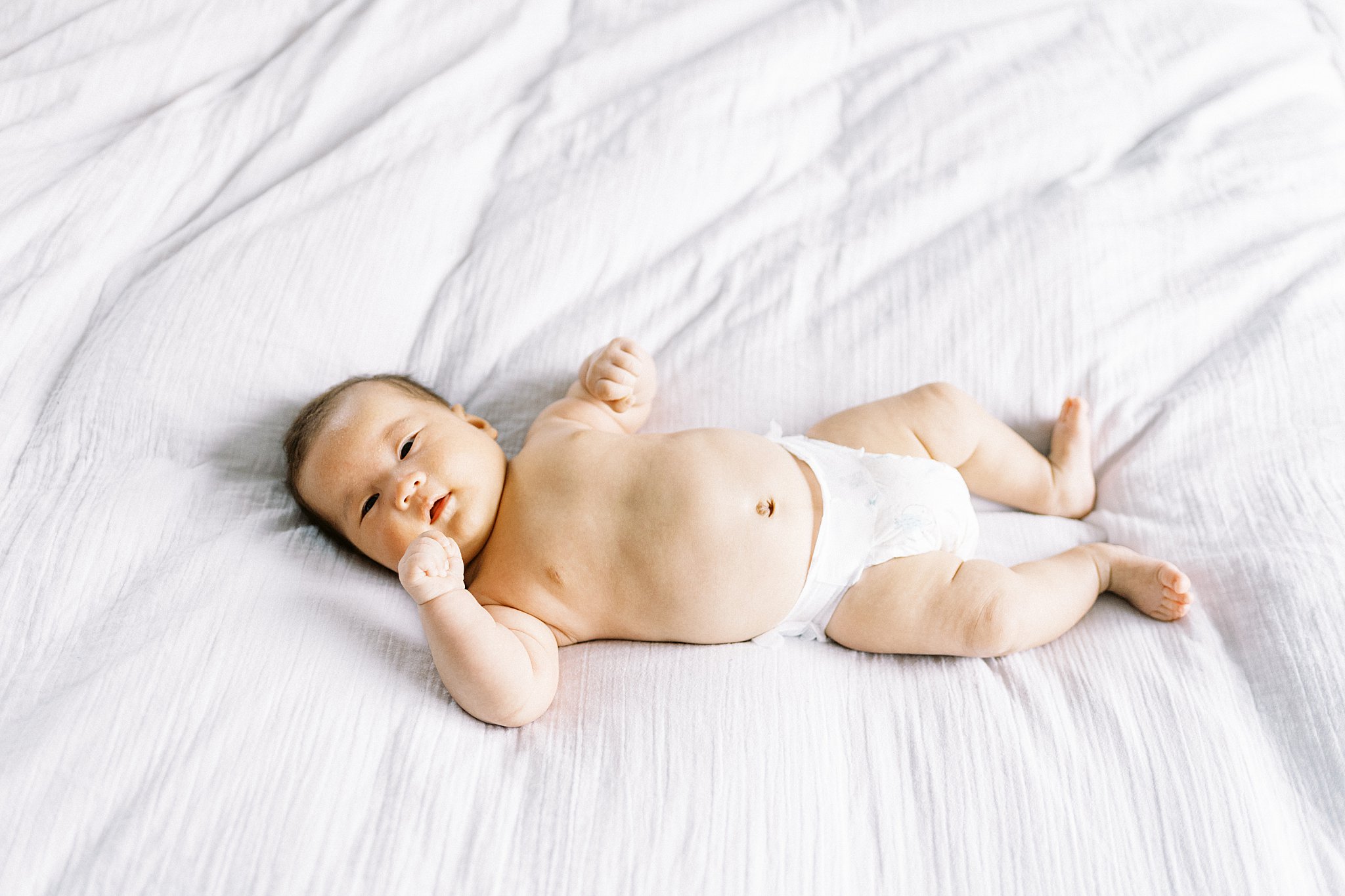 little one lays on bed in diaper by Lynne Reznick Photography