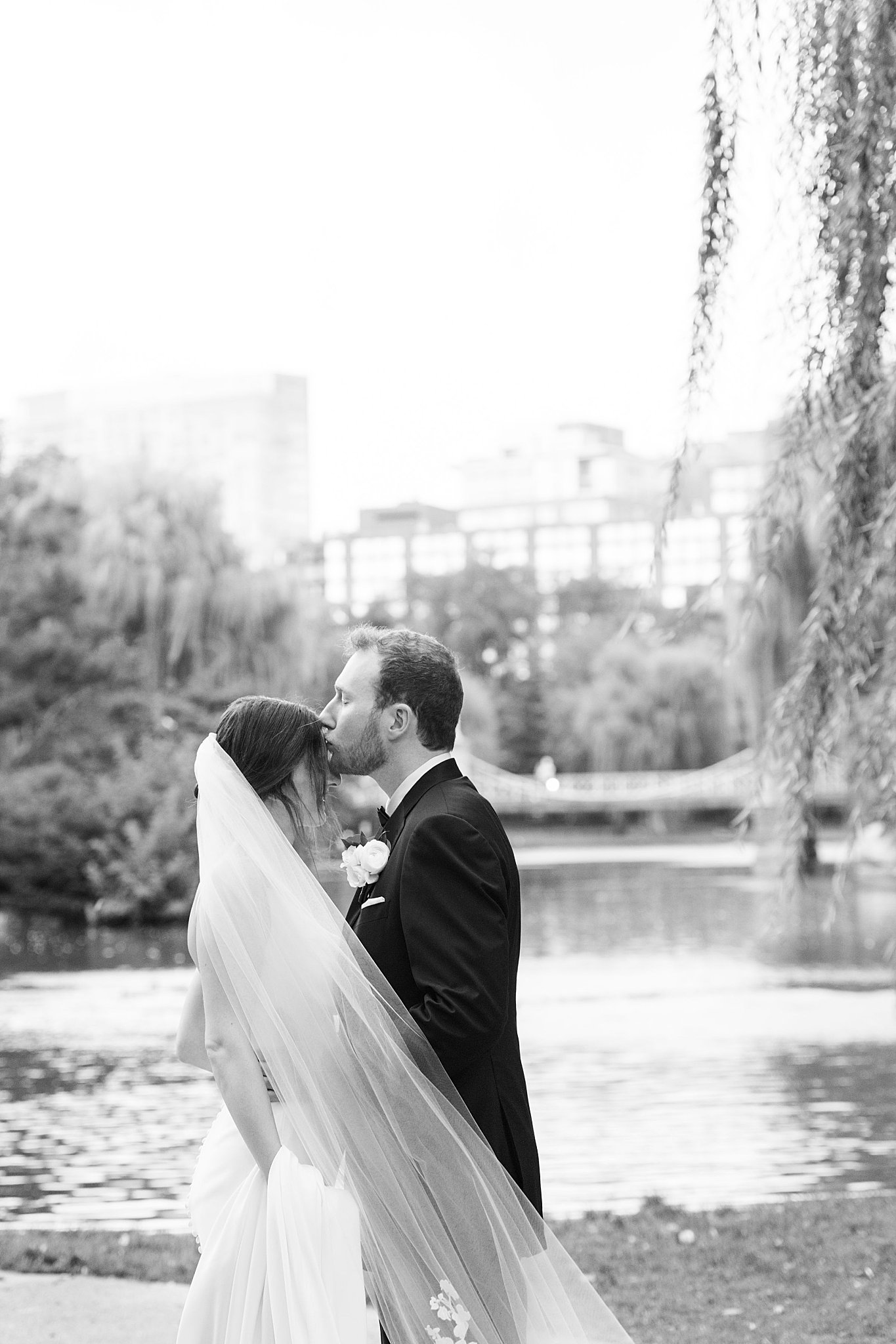 man kisses woman on forehead as he veil blows in the wind by Lynne Reznick Photography