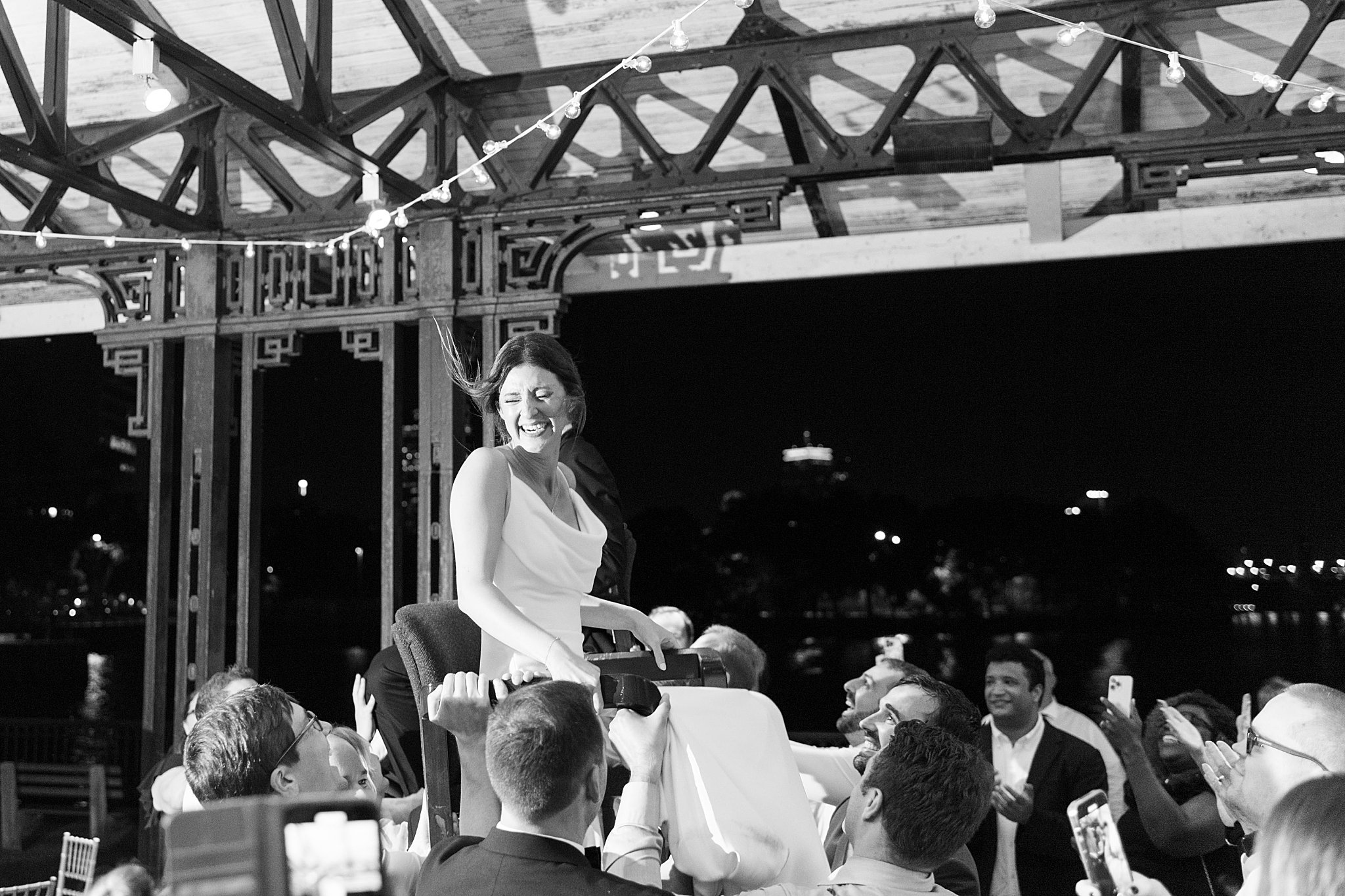 woman laughs as she is held up in a chair by Boston Wedding Photographer