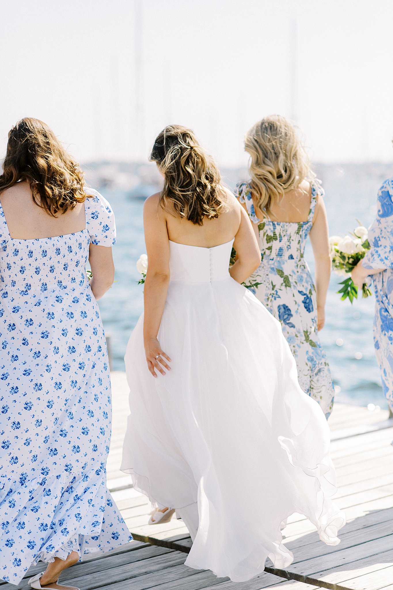 bridesmaids in mismatched white and blue dresses walk with bride at The Bohlin