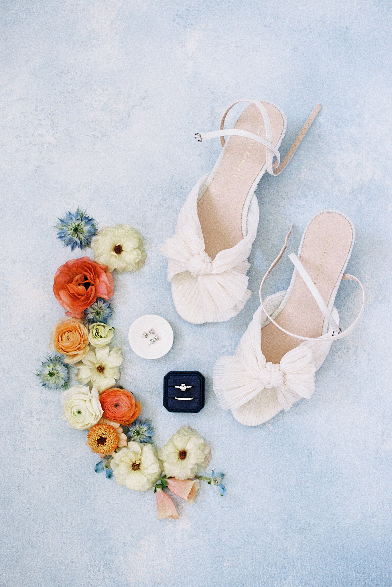 bride's shoes, rings, and earrings with flowers around at The Bohlin