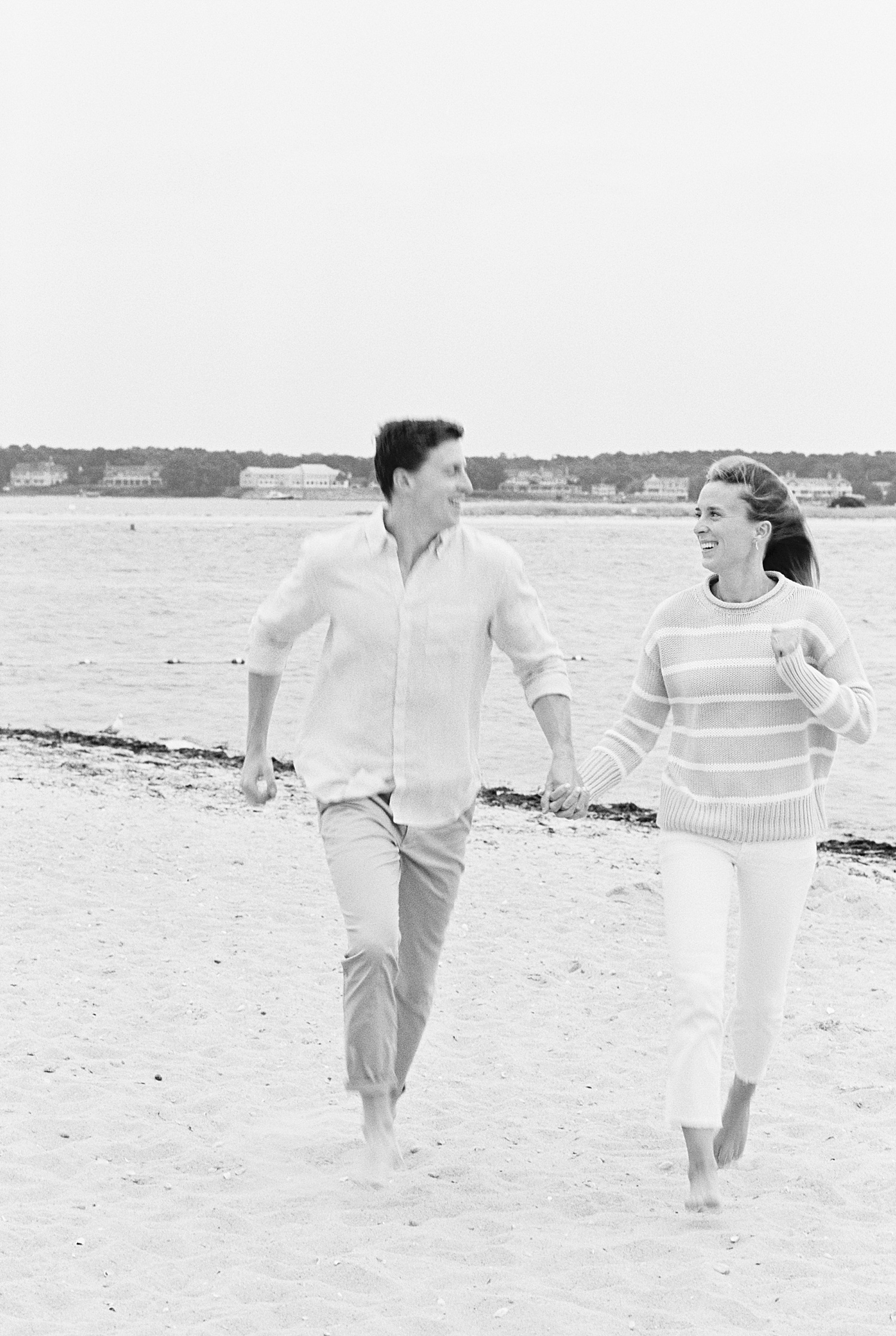 man and his fiancé run in the sand, laughing together by Lynne Reznick Photography