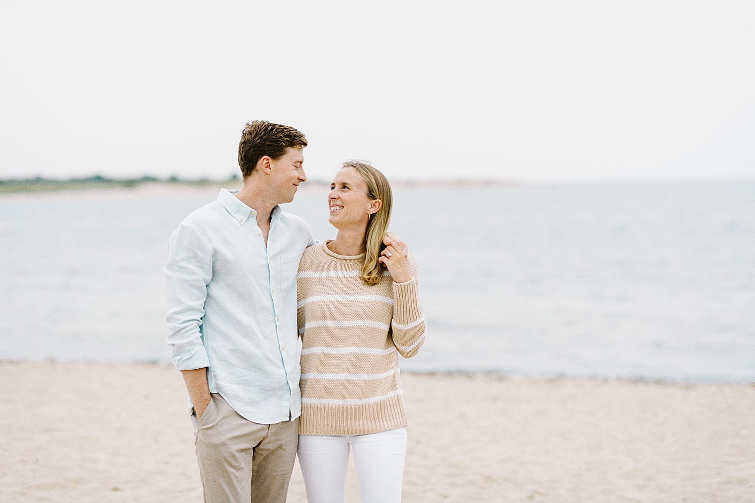 blonde woman looks adoringly at her fiancé on the shores of Cotuit Bay