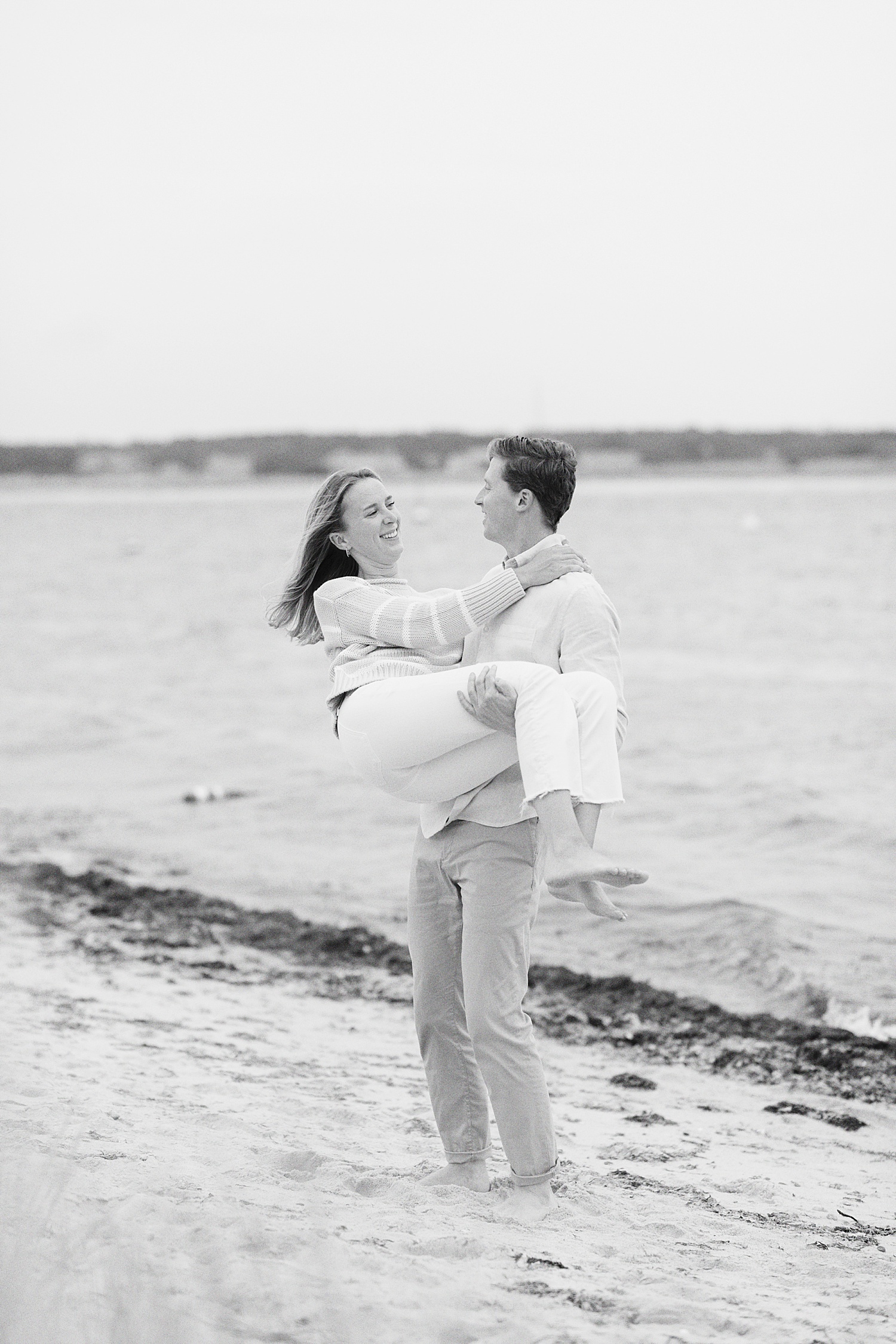 groom-to-be picks up woman to twirl her on the sand by Cape Cod Wedding Photographer