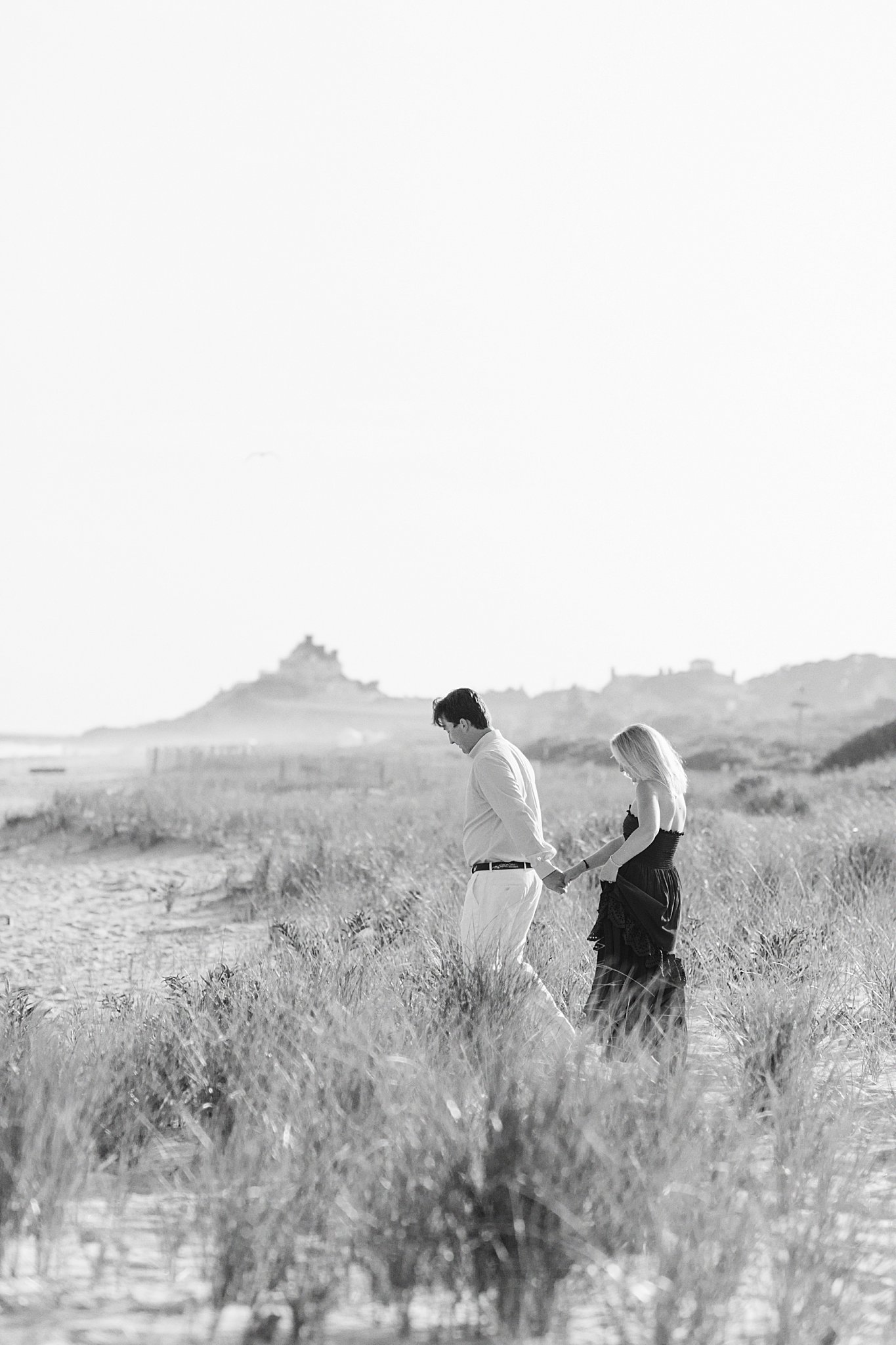 man leads woman through grass along beach by New England wedding photographer