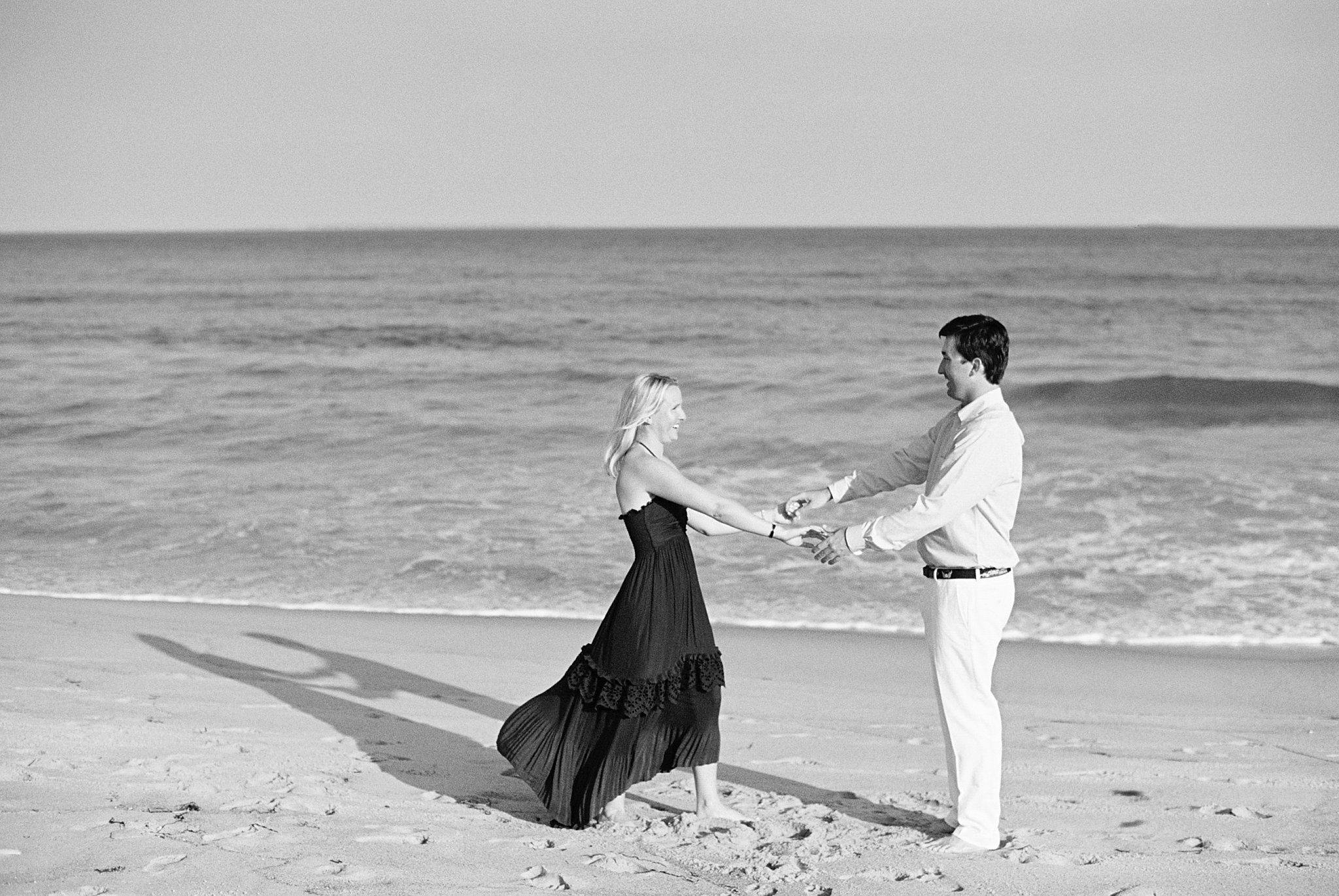 man and woman hold outstretched hands at beach by New England wedding photographer