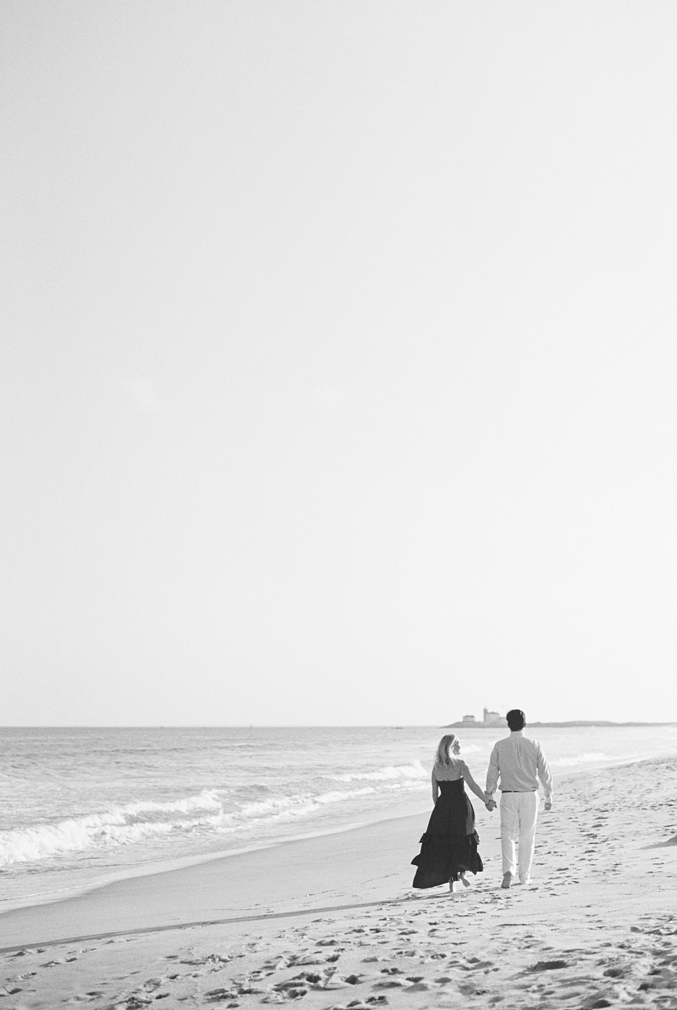 couple walks hand in hand along the shore by Watch Hill engagement session