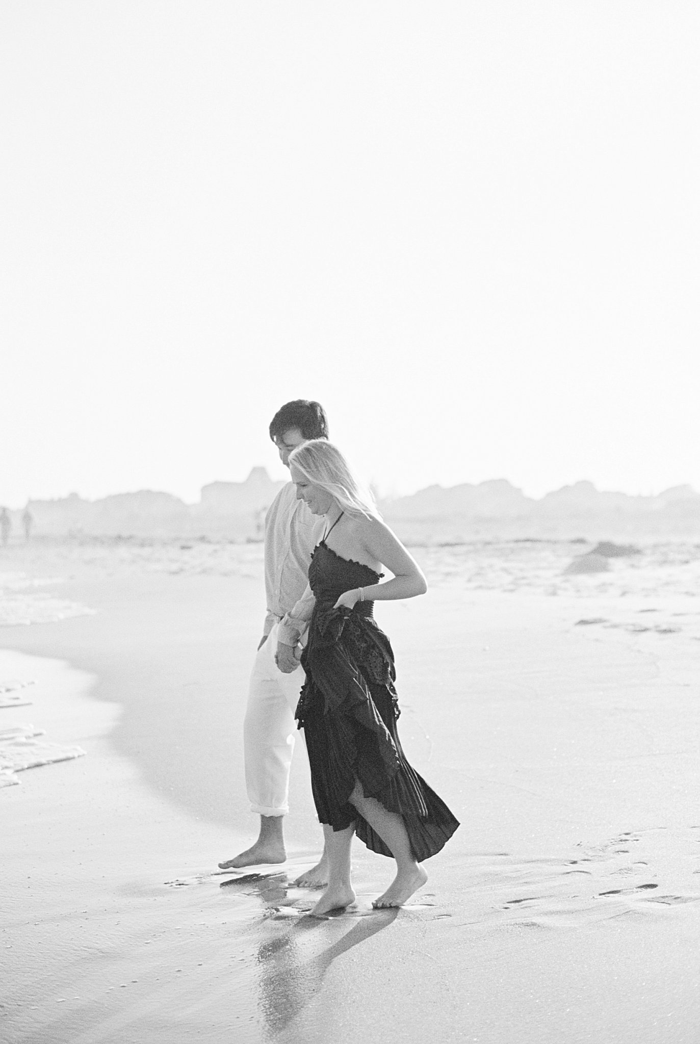 woman holds up skirt as couple puts toes in water by New England wedding photographer