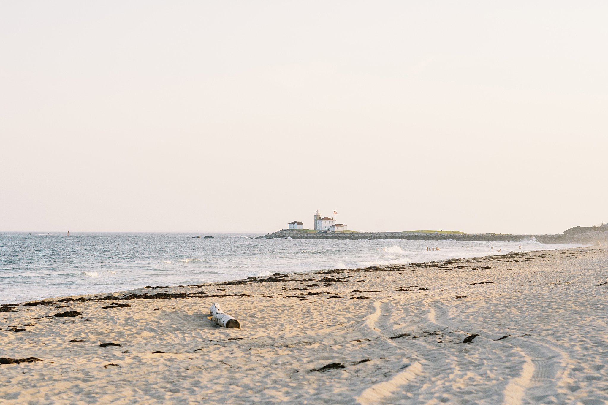 lighthouse is off in distance across beach at Watch Hill engagement session