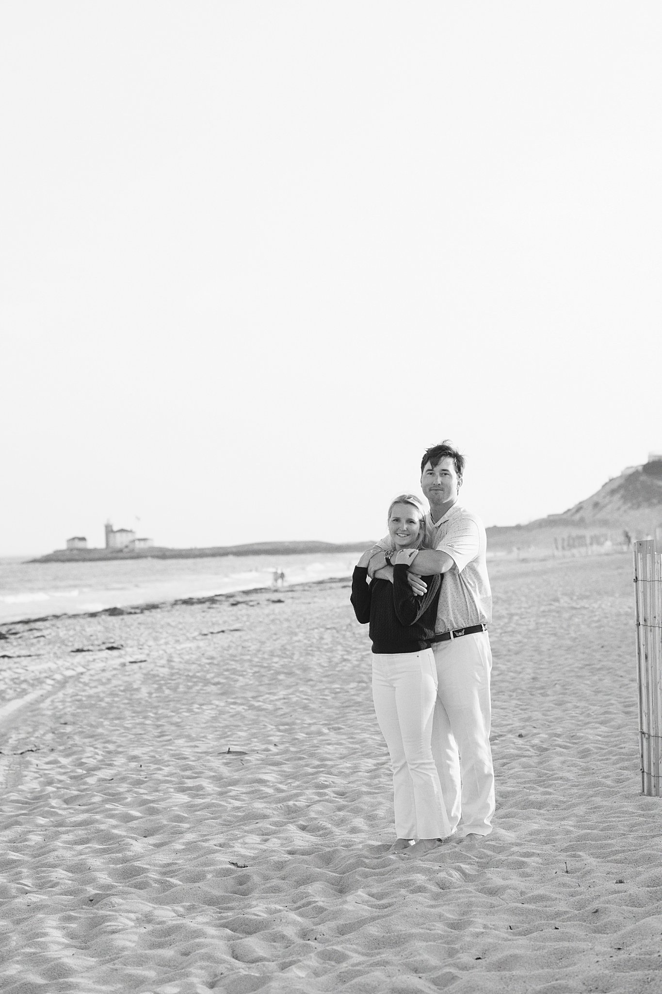 man wraps arms around woman on sand by New England wedding photographer