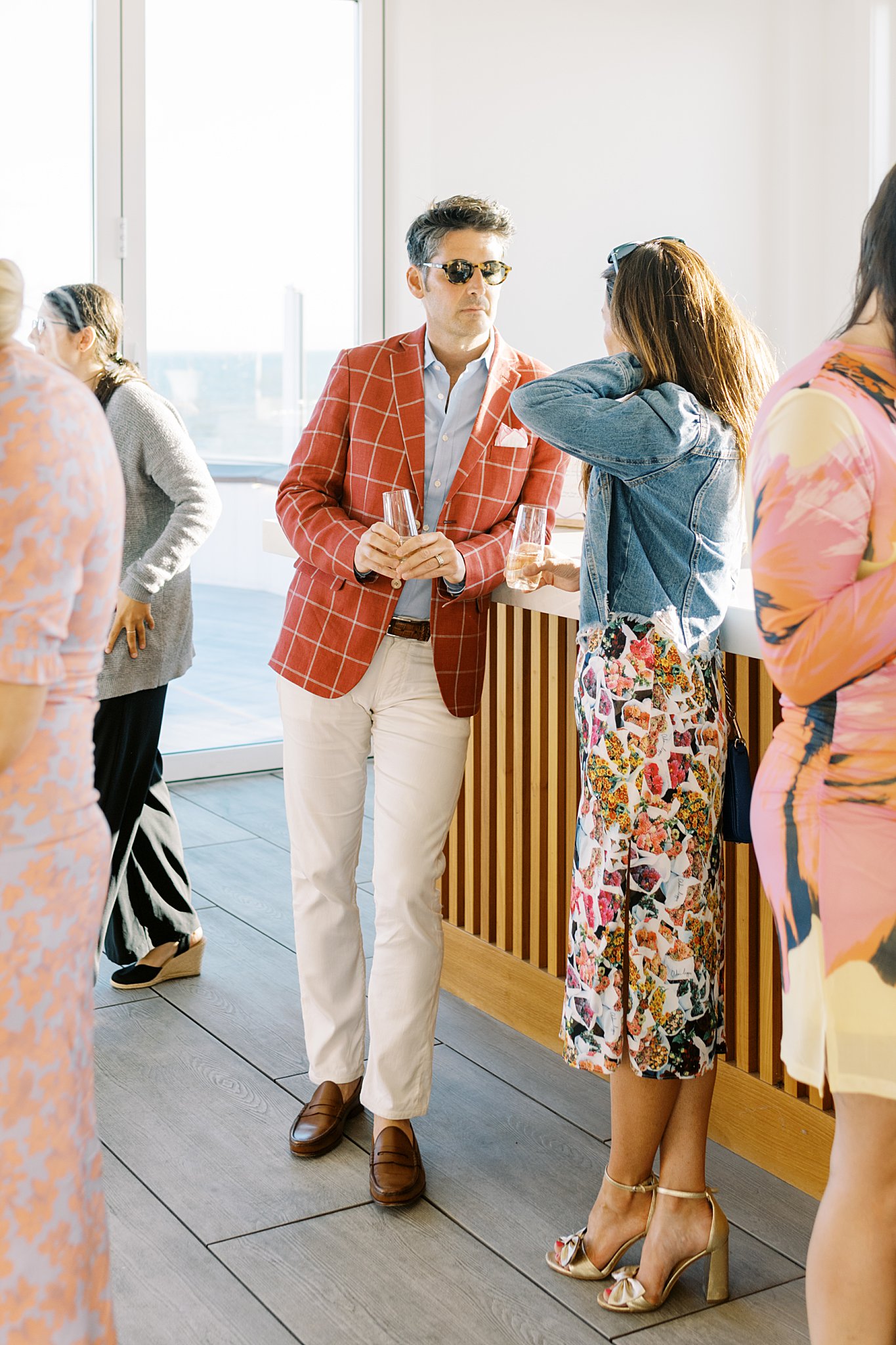 man in rust suit coat and sunglasses leans on the bar talking to a woman by Cape Cod wedding photographer