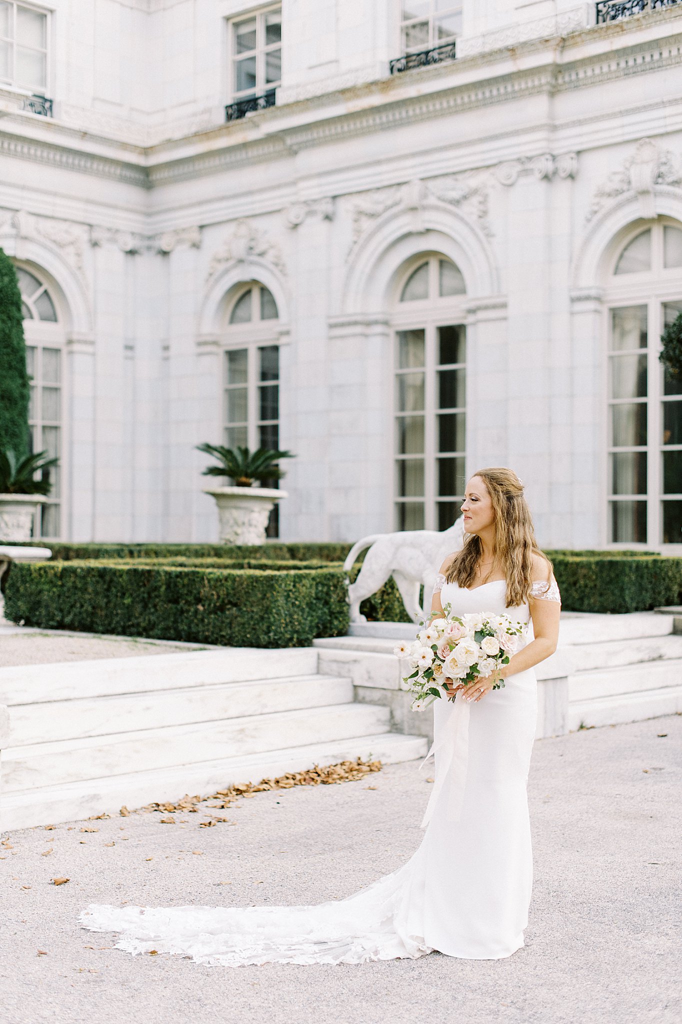 bride stands outside mansion with bouquet by New England wedding photographer