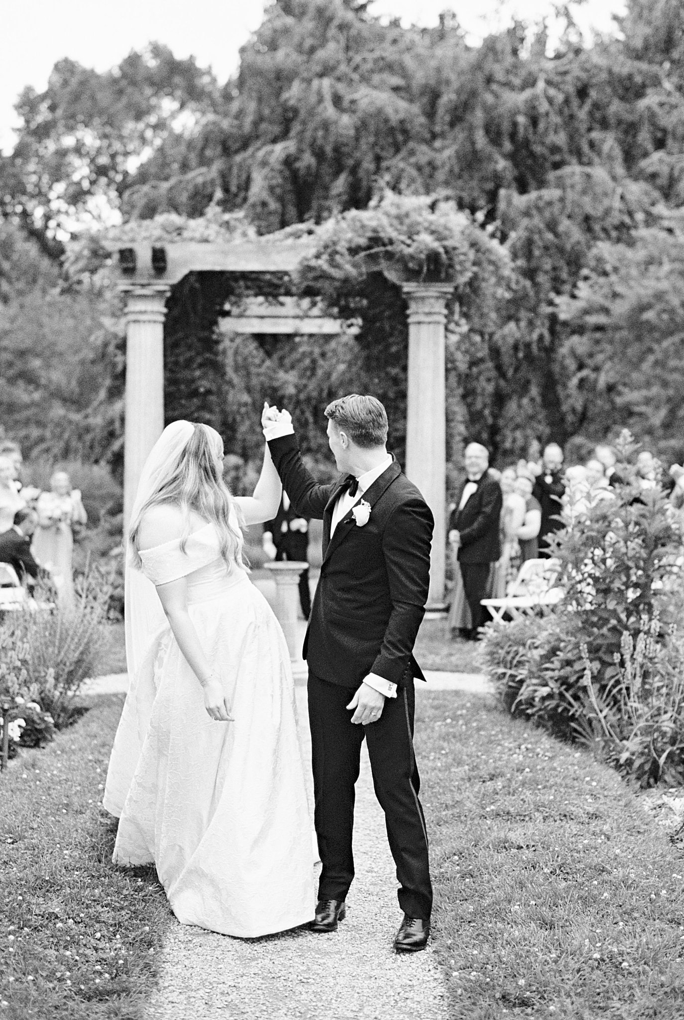 newlyweds lift arms as they look at guests by Boston wedding photographer