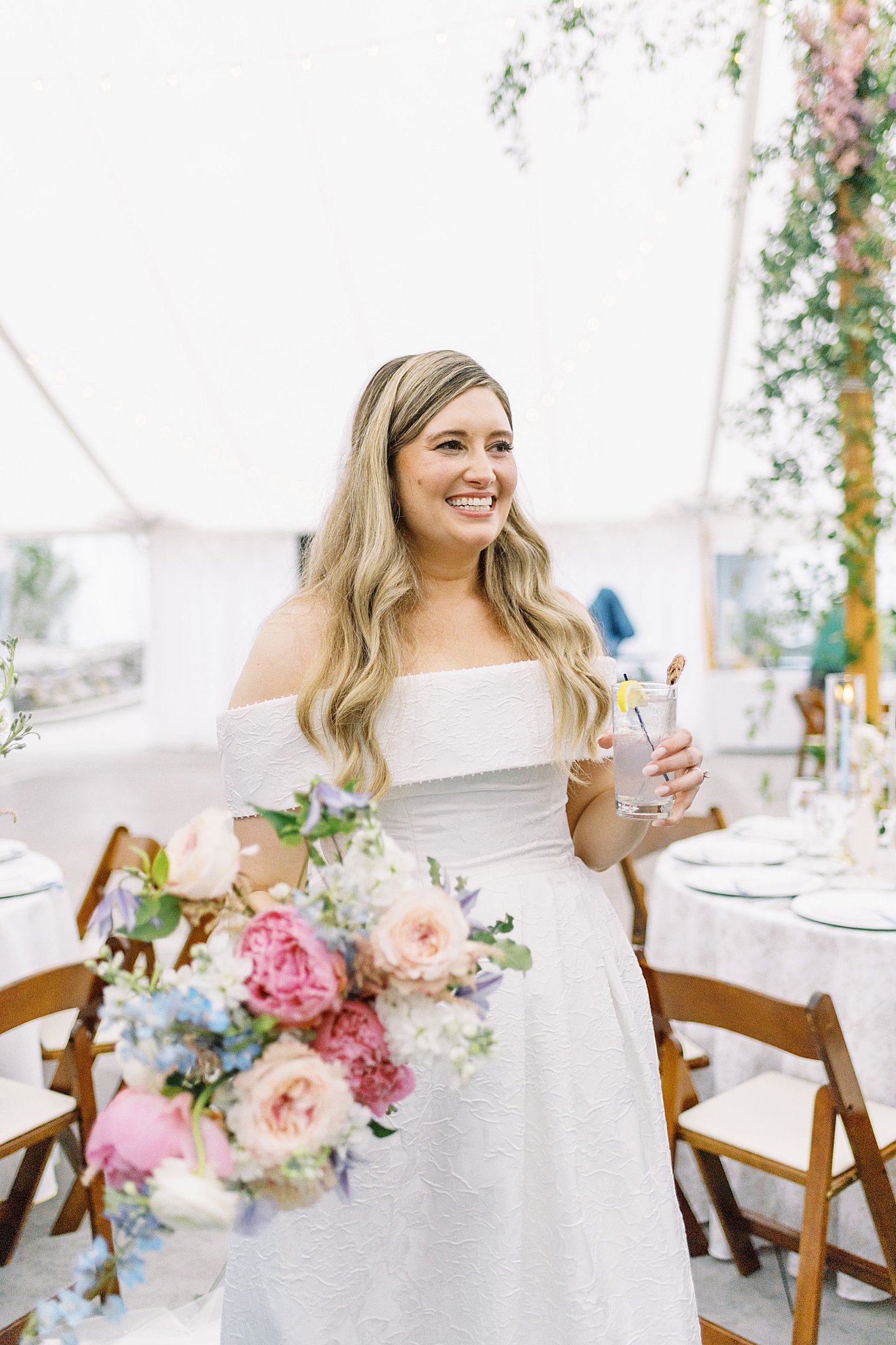 bride sips a cocktail in a white tent at Glen Magna Farms