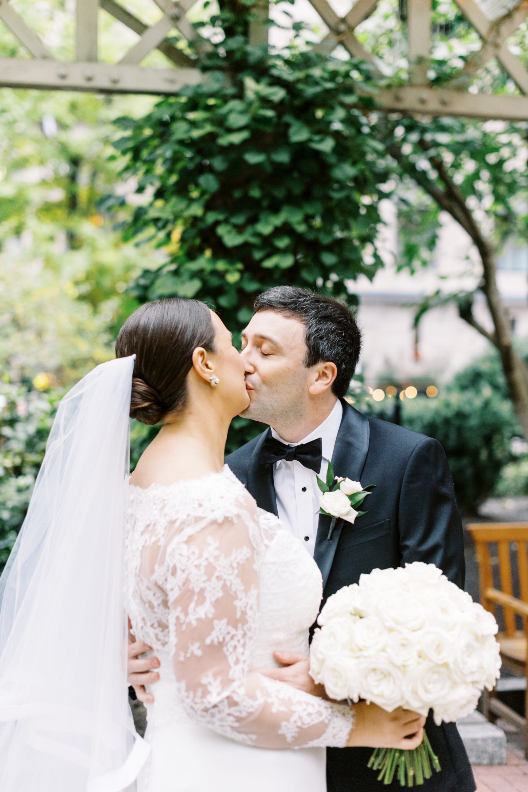 bride in vera wang gown with lace sleeves kisses her groom under arbor in the heart of Boston during their first look on their wedding day at The Langham Hotel