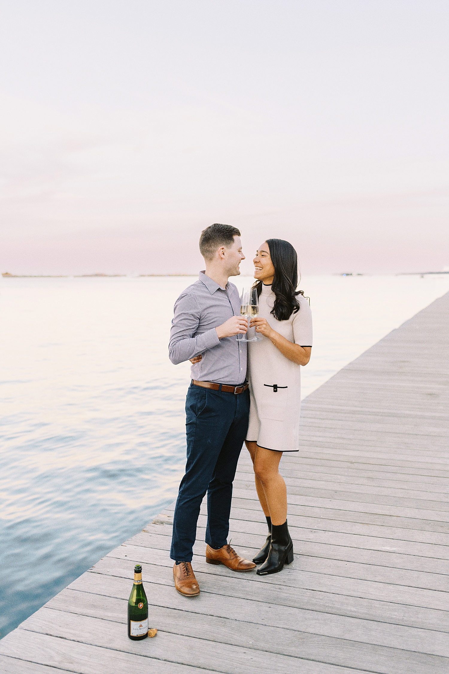 man and woman share a toast by water for Fan Pier Park Engagement Session