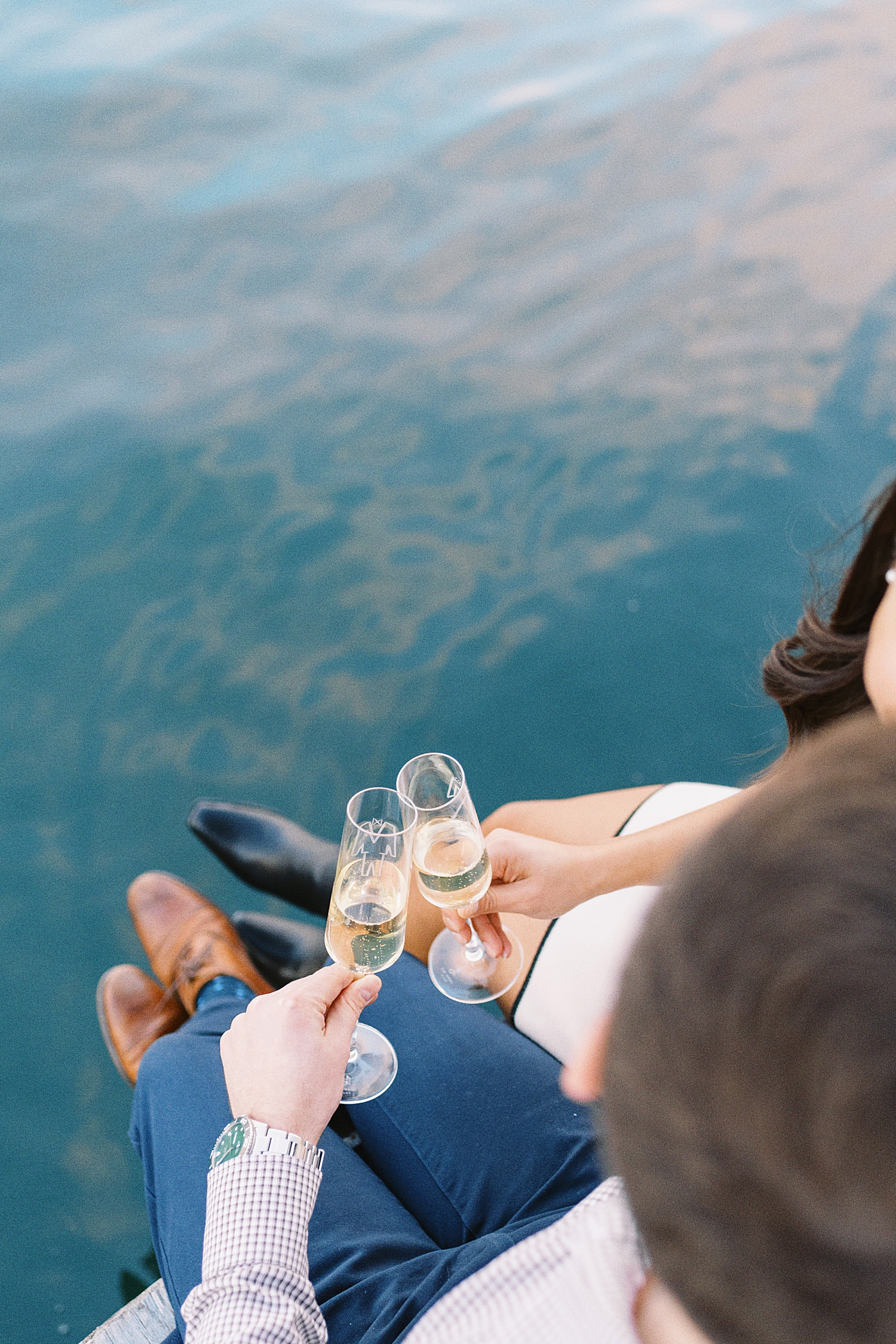 couple holds bubbly while sitting on pier by Lynne Reznick Photography