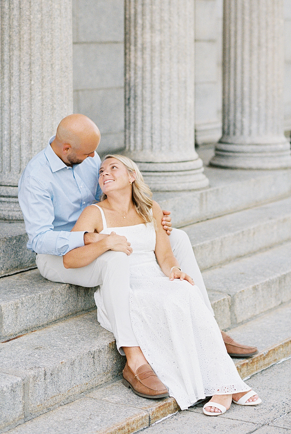 Man smiles at woman while they sit on the steps during their Charlestown Engagement Session 