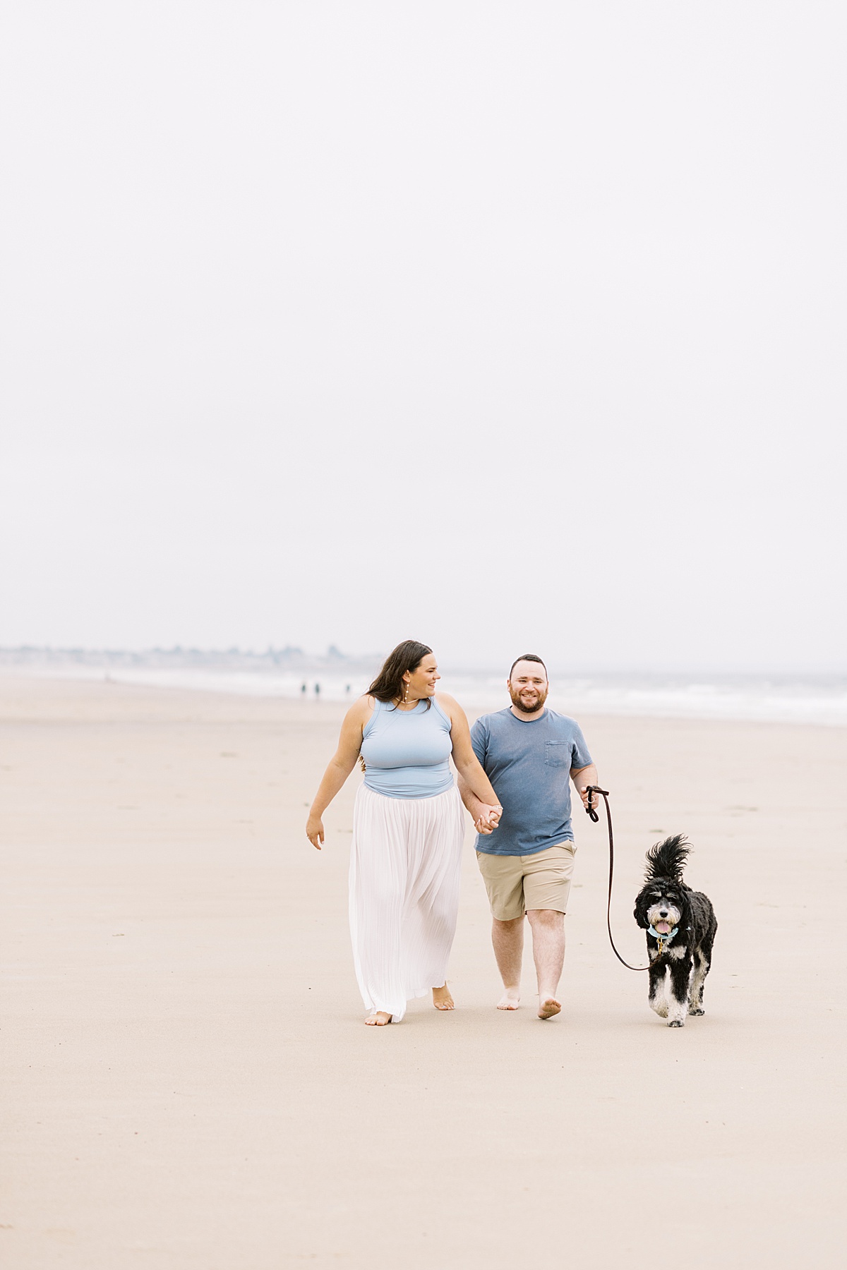 Couple walk hand in hand together with their dog on Footbridge Beach 