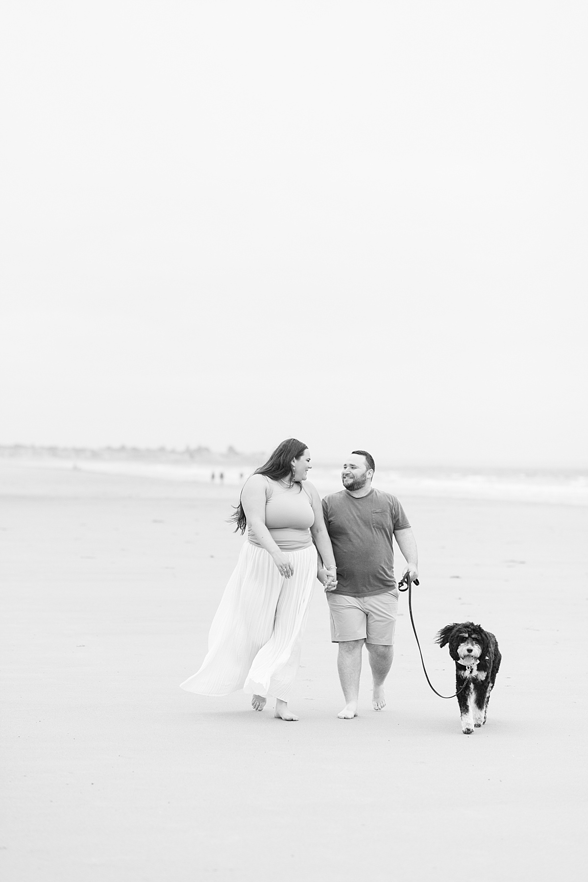 Man and woman walk together with their dog on the beach by Coastal Maine Wedding Photographer