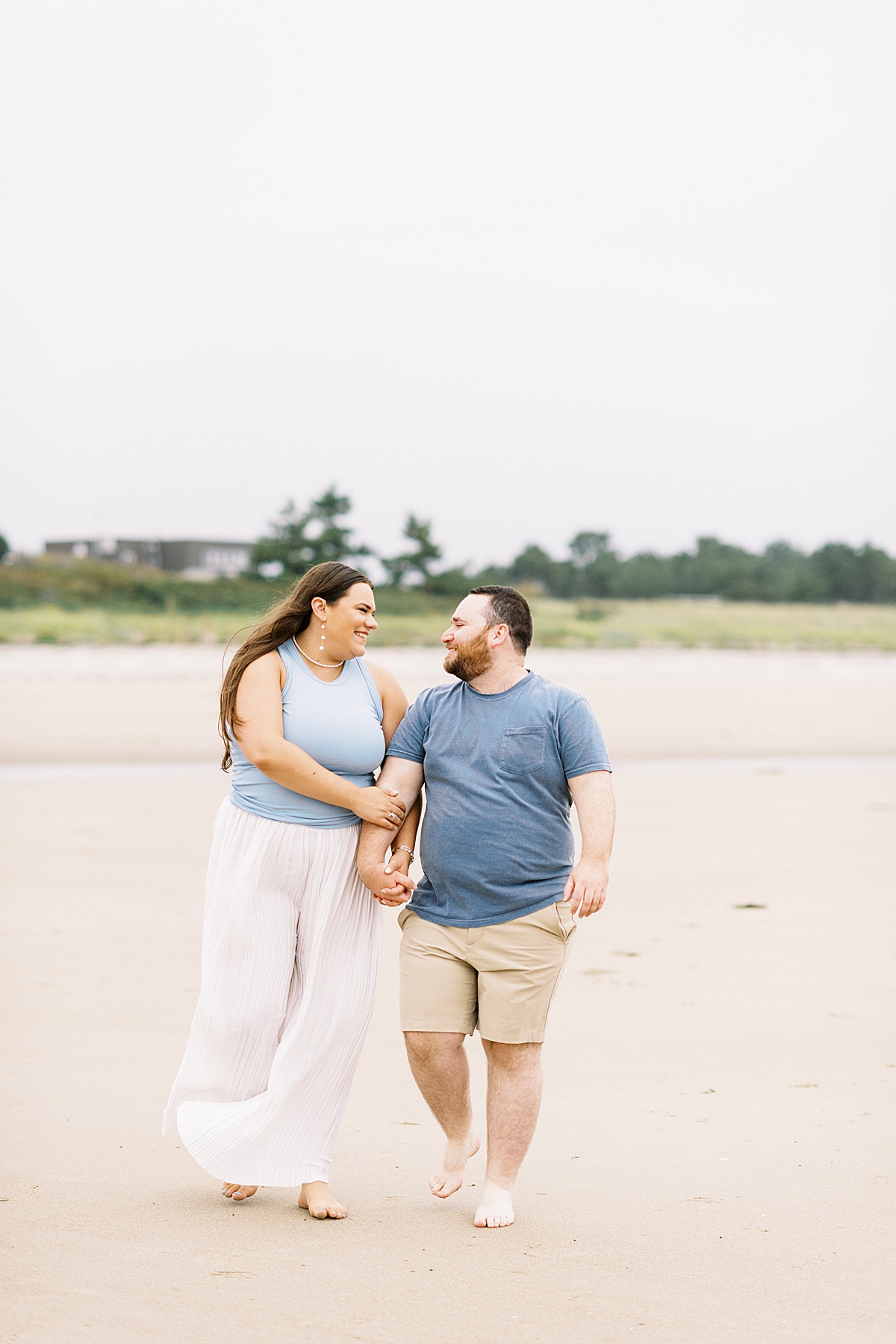 Engaged couple smile at one another with their hands intertwined on Footbridge Beach 