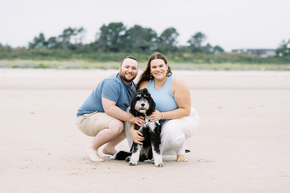 Couple smile together holding their pup for Coastal Maine Wedding Photographer