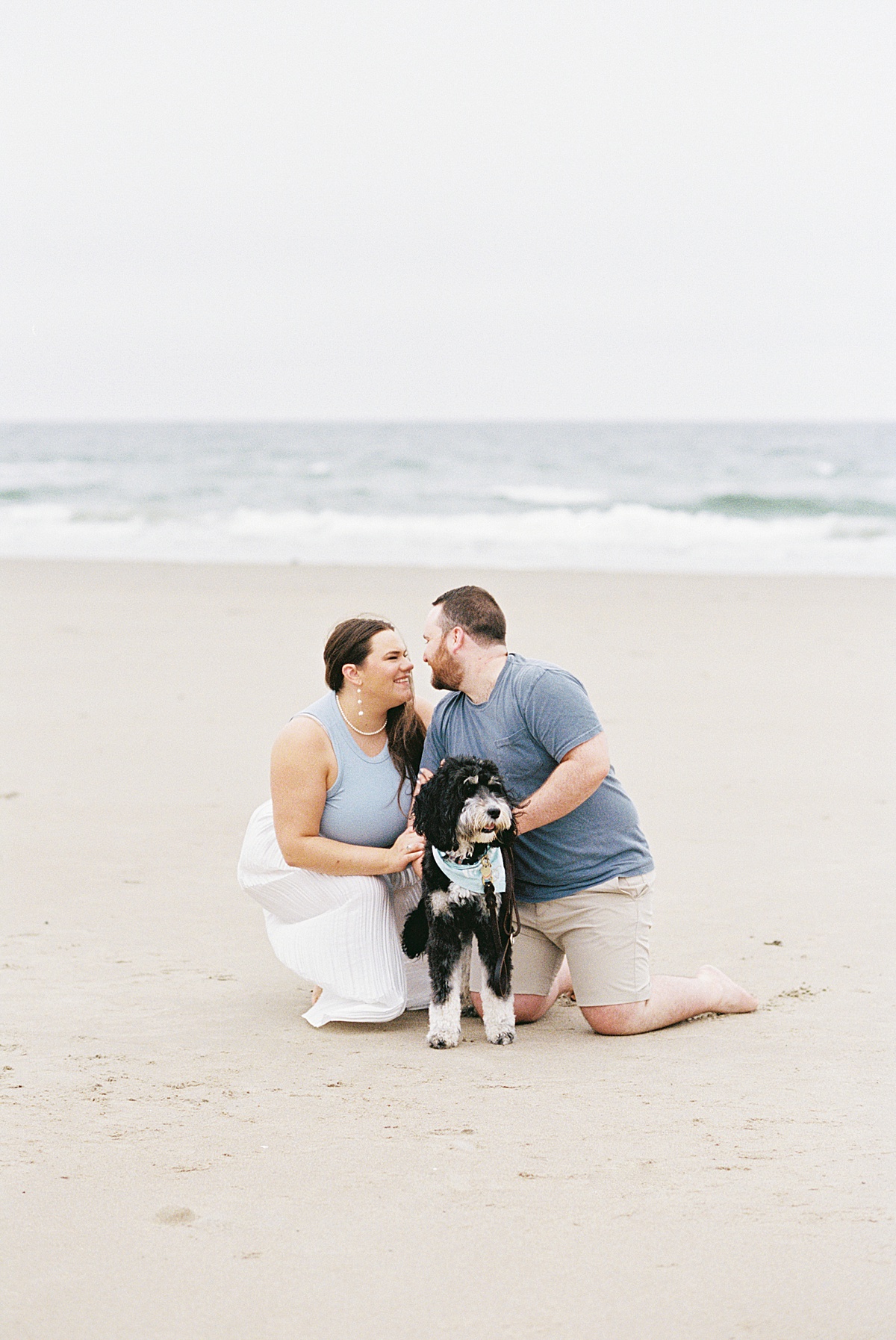 Man and woman kneel down on the beach together for Coastal Maine Wedding Photographer