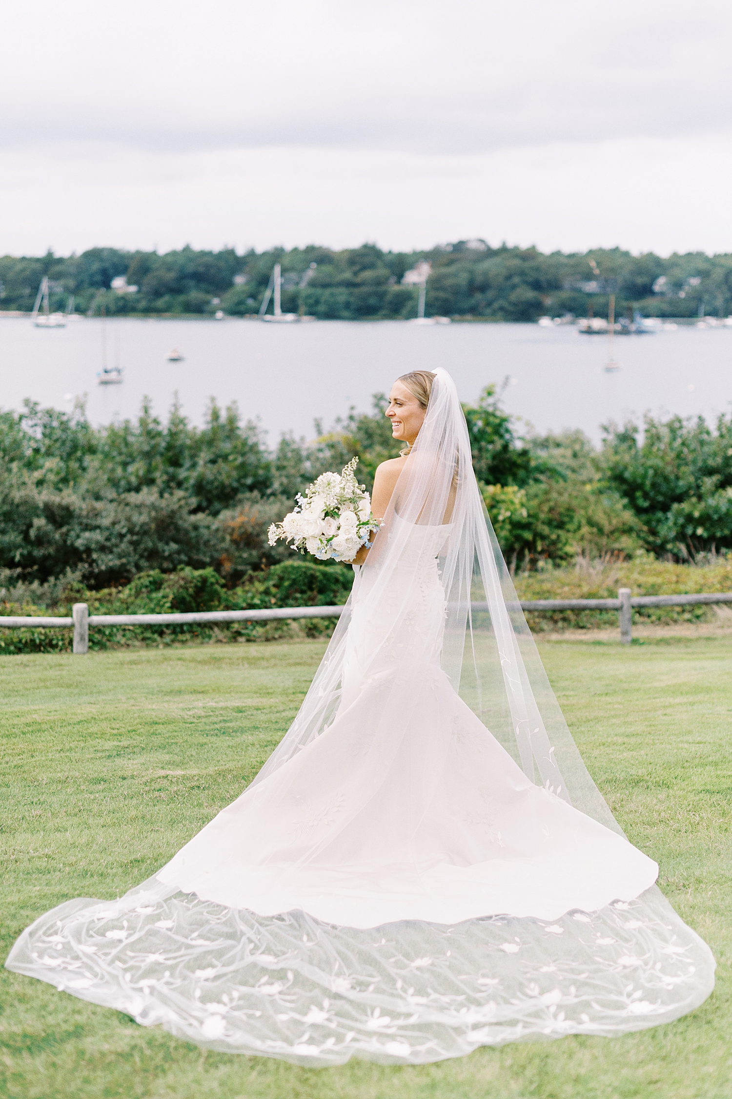 woman in long white dress and veil looks over the water at Oyster Harbors Club