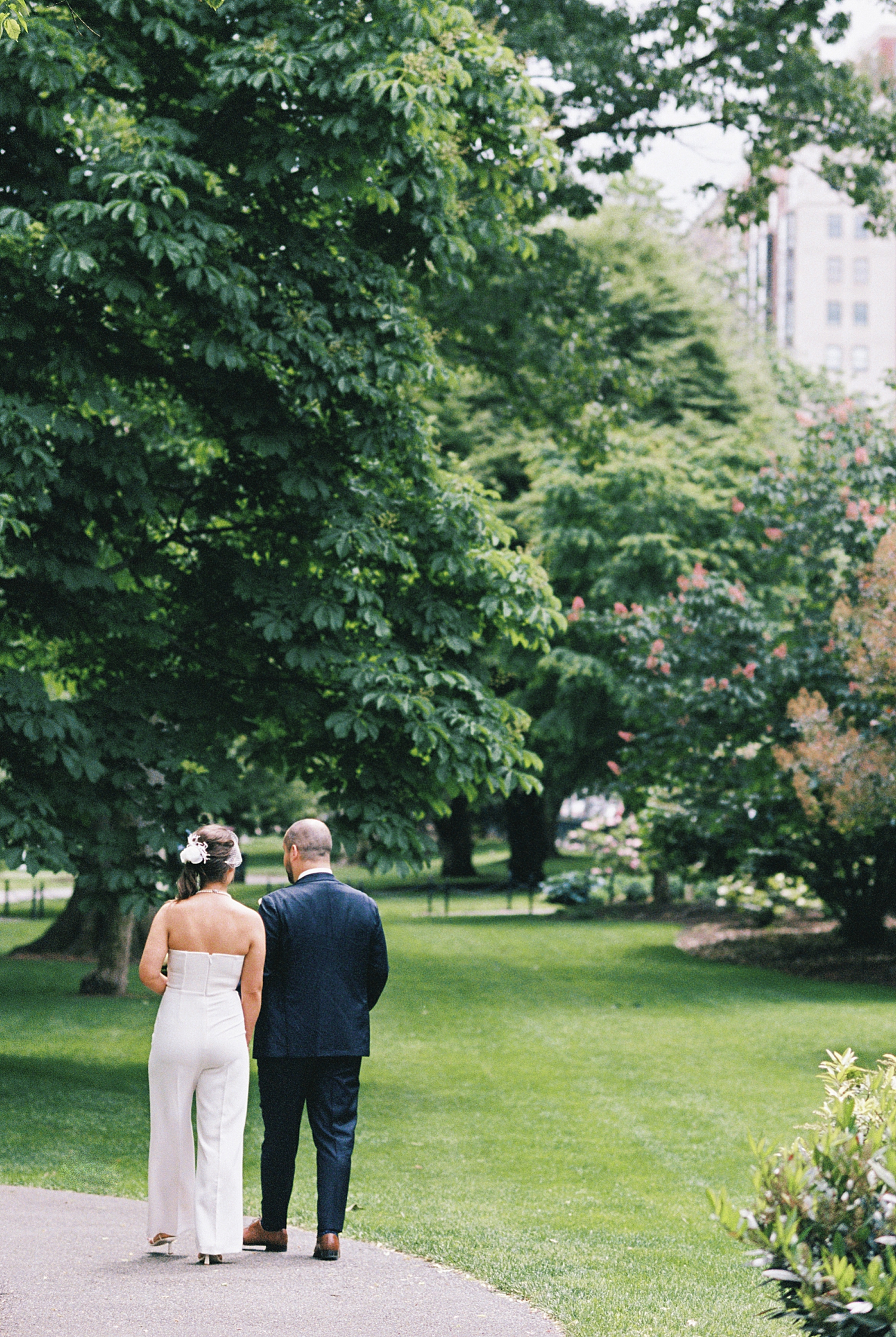 husband and wife stroll through green trees at Boston Public Garden