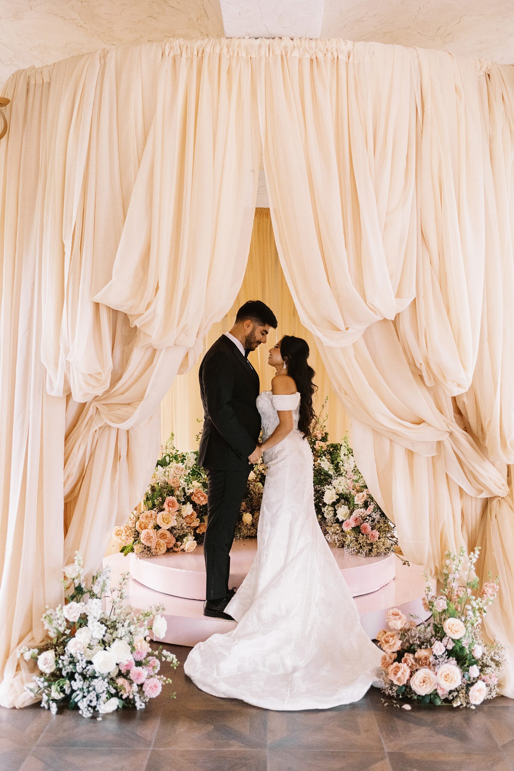 peach drapery and lush florals with couple saying vows at Villa Antonia wedding