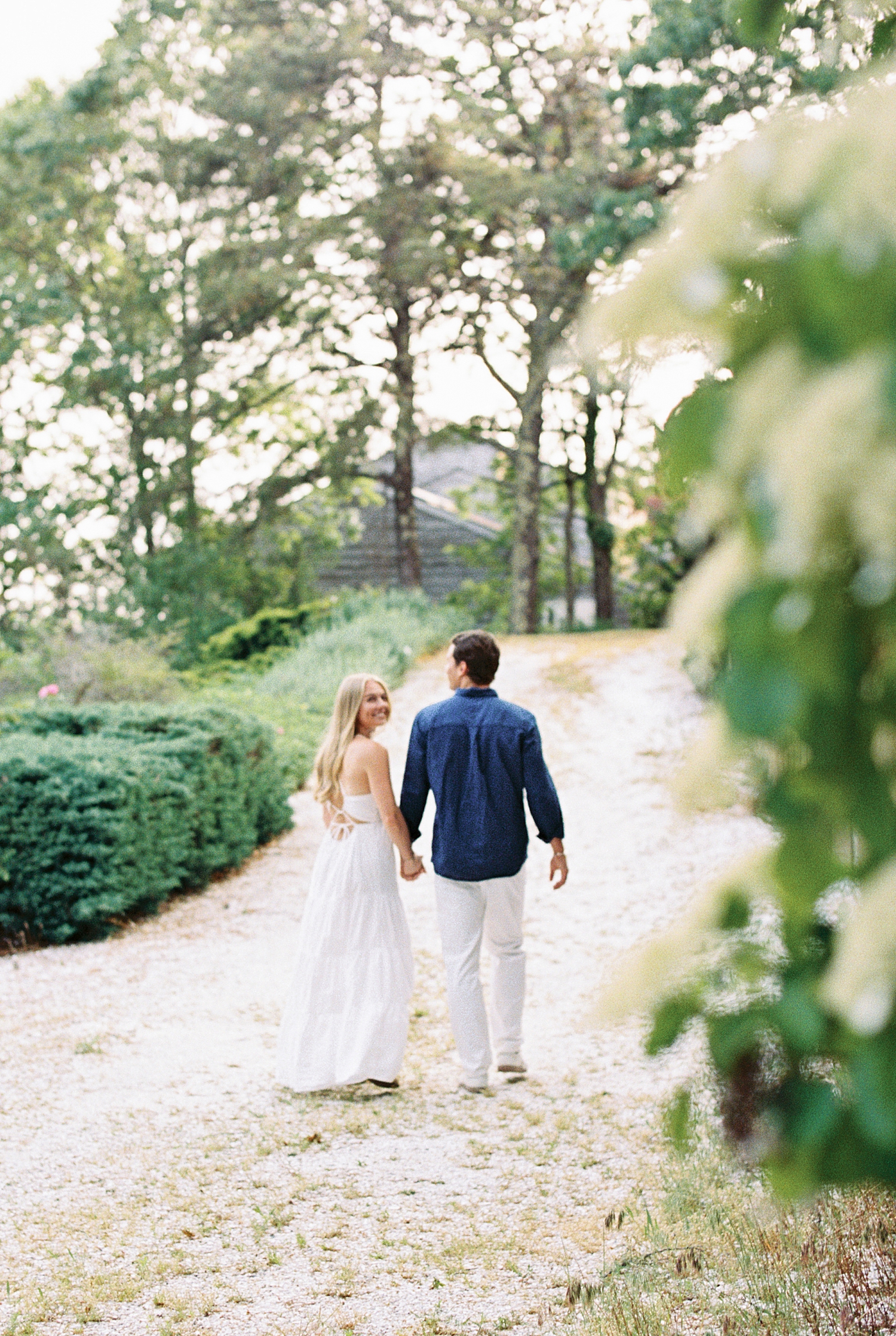 woman looks back over her shoulder walking down path with her fiancé by Lynne Reznick Photography