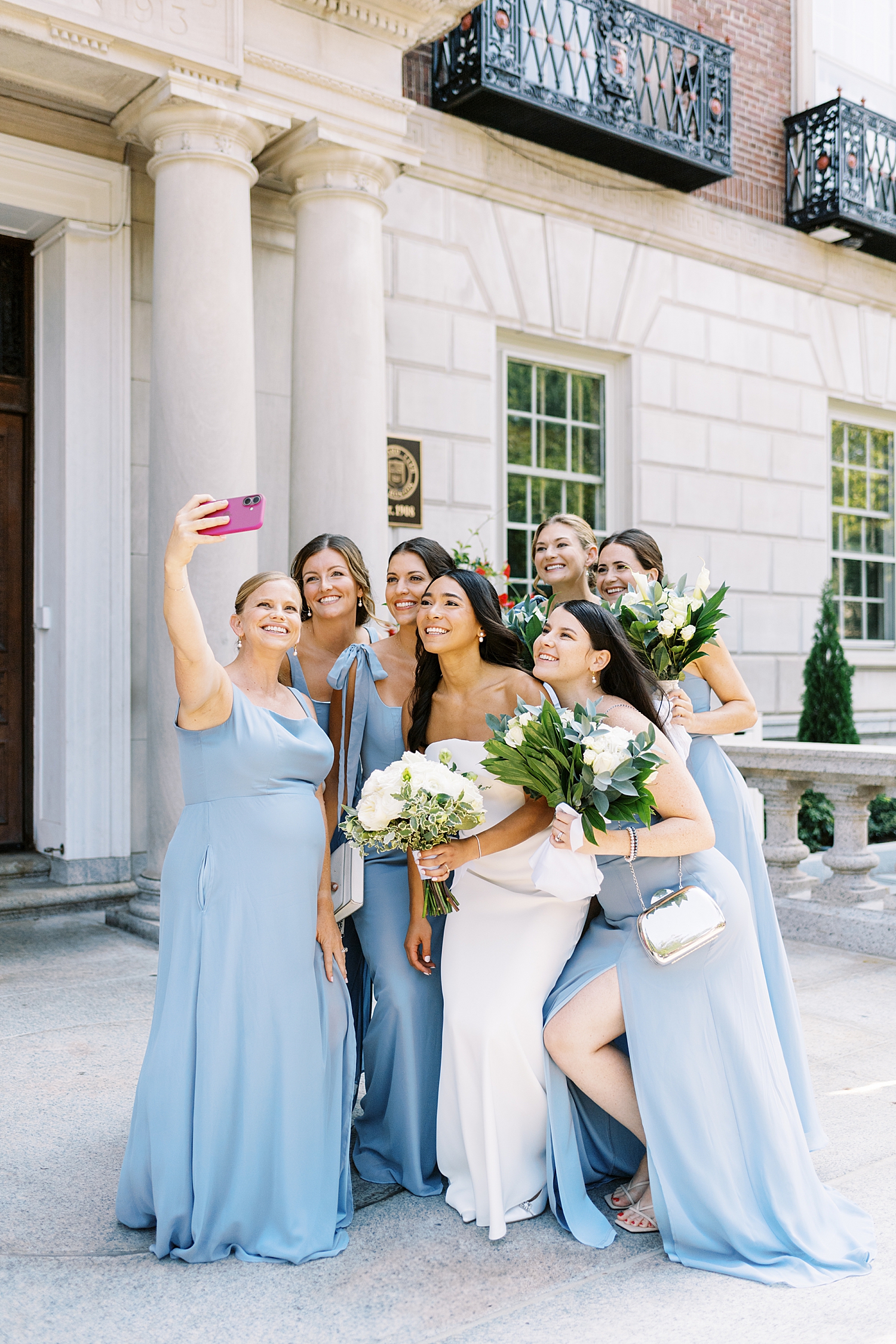 bride leans down to take a selfie with bridesmaids near Havard Club of Boston