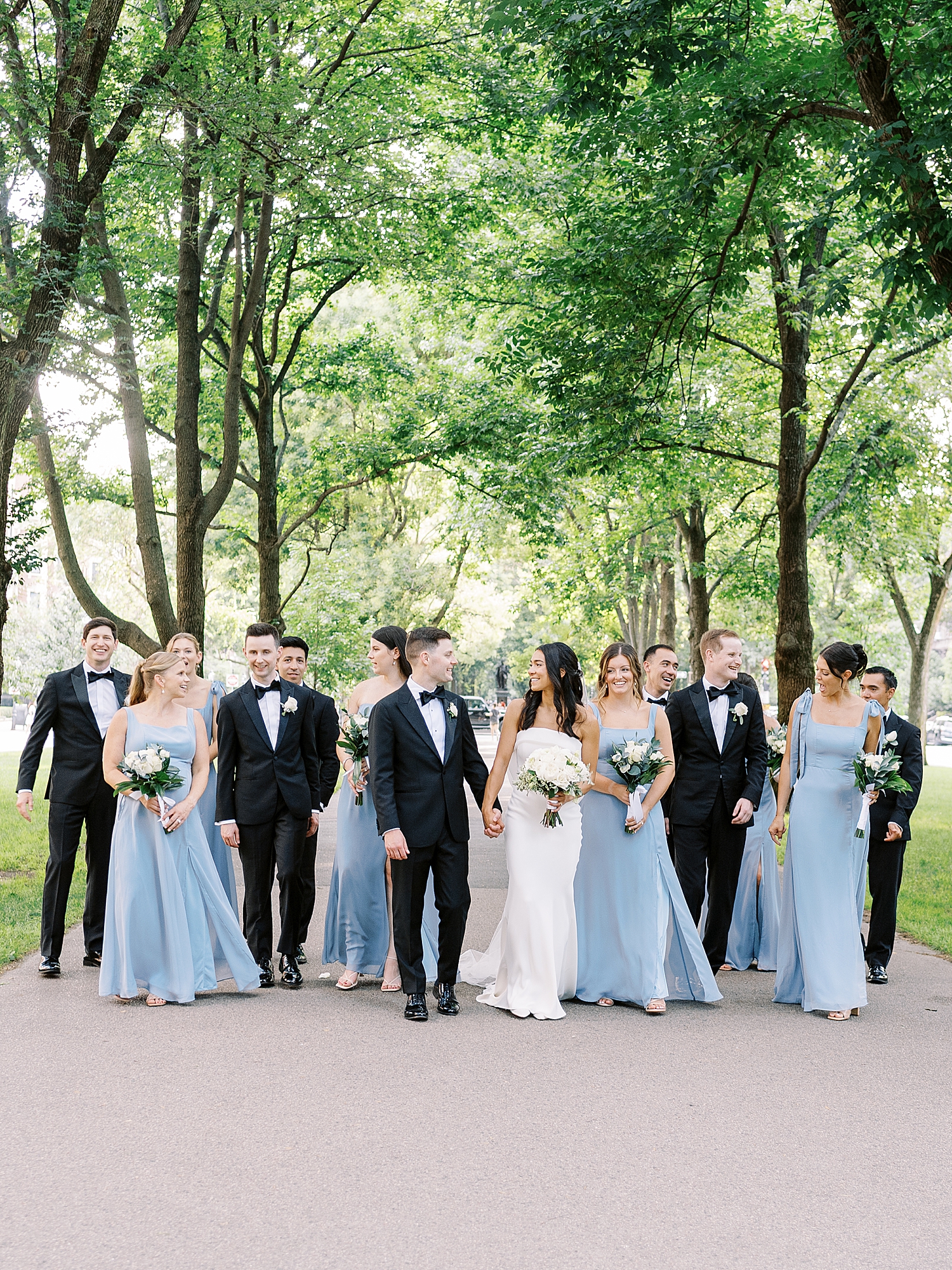 bride and groom walk through the park with their bridal party near Havard Club of Boston