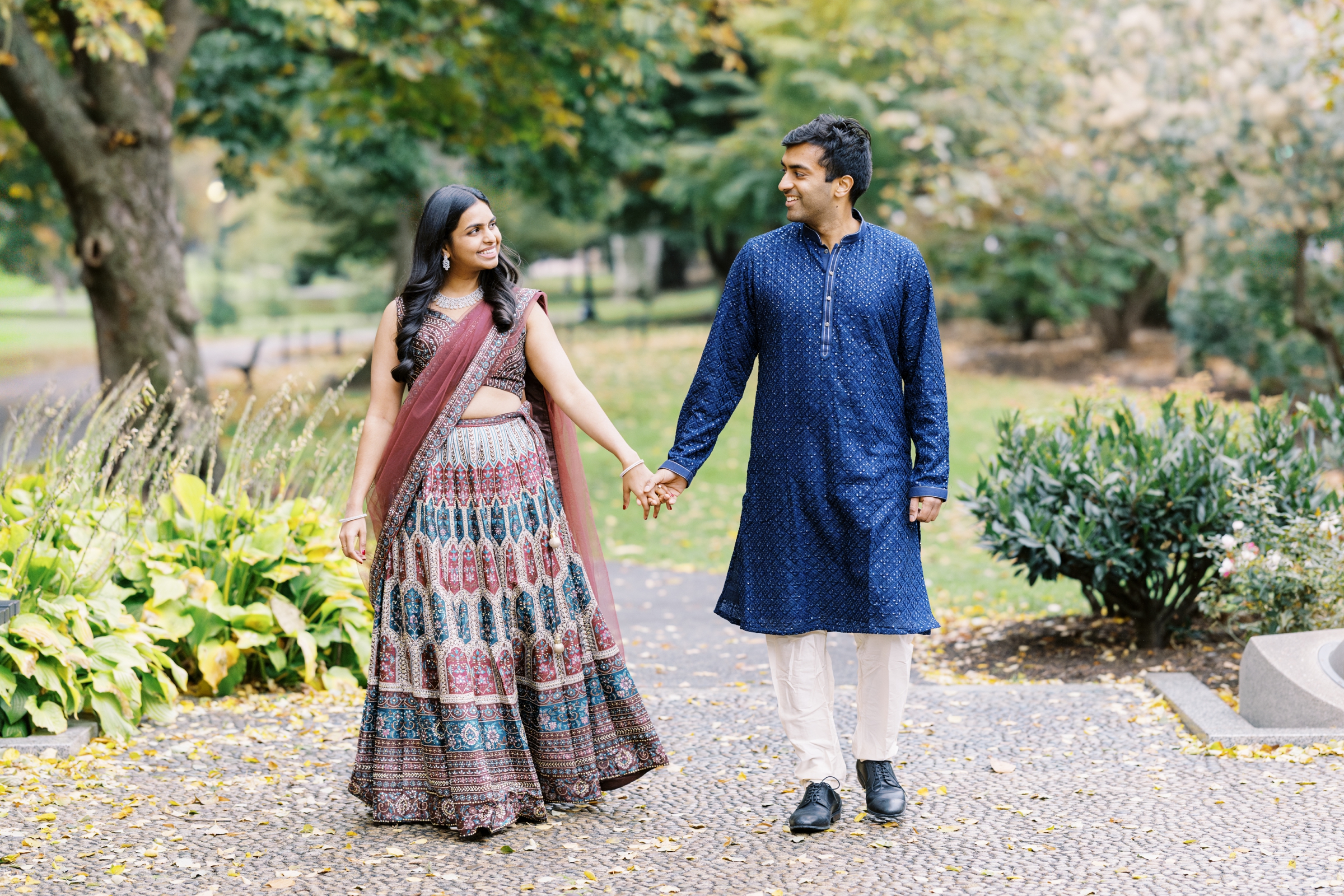 Indian couple walks holding hands during fall Public Garden engagement session by associate photographer for Lynne Reznick Photography