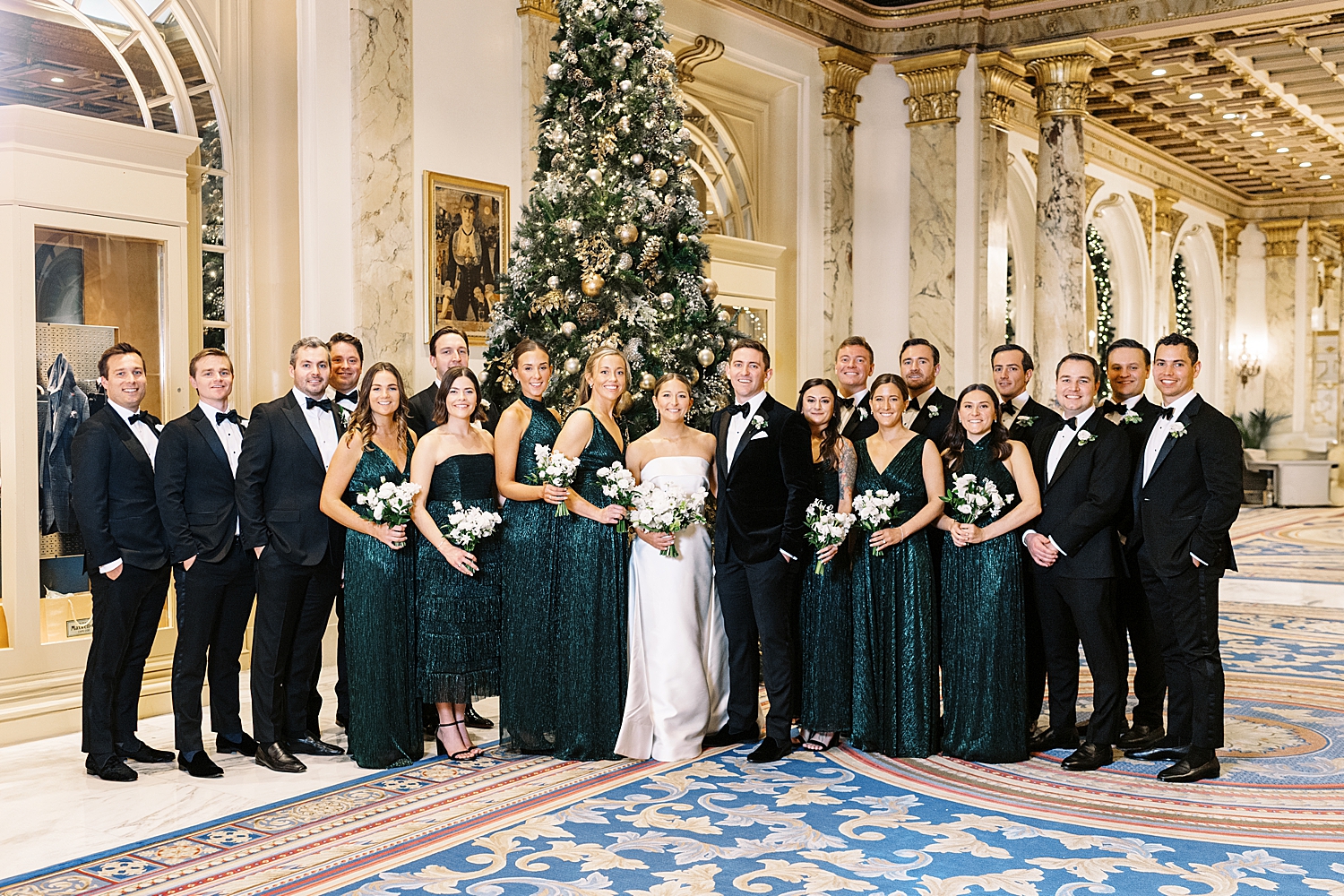 bridal party in velvet dresses and men in tuxes in front of christmas tree for NYE wedding weekend